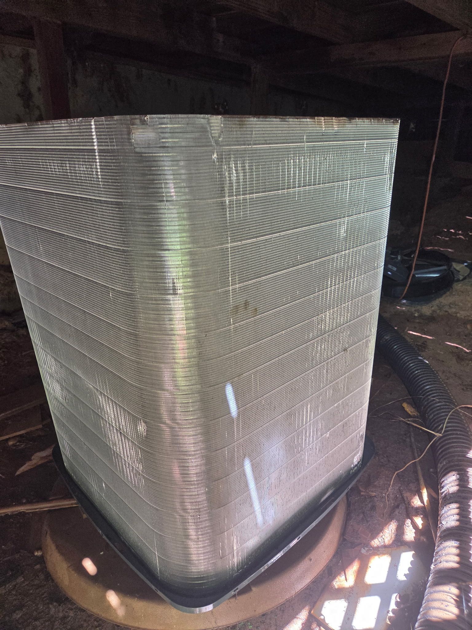 Large silver metal HVAC filter leaning in a dark interior space, lit by sunlight from the side