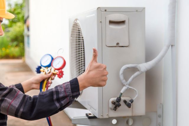 Technician giving thumbs up beside an outdoor air conditioner unit with gauges attached