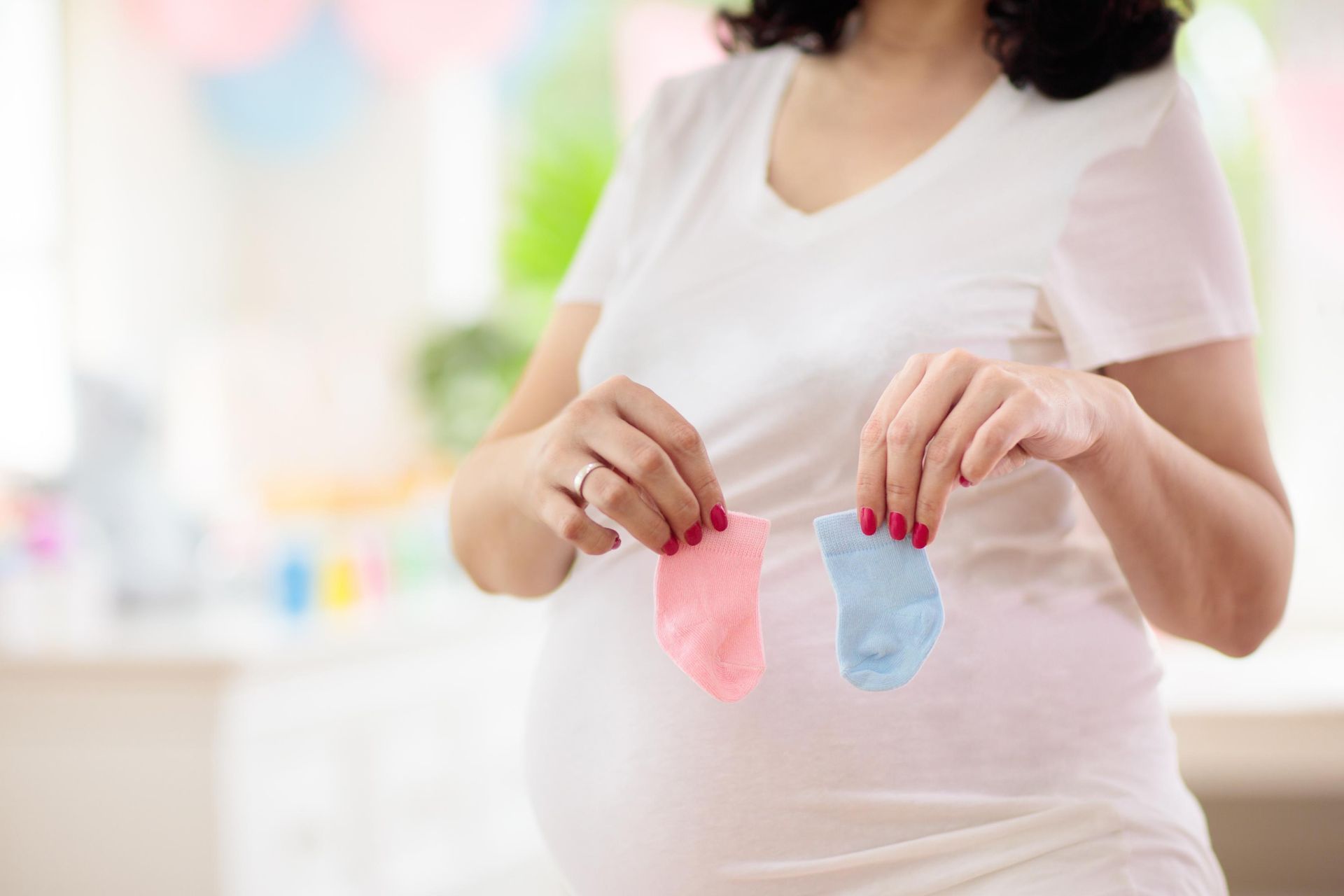 Pregnant woman holding pink and blue baby socks, possibly for a gender reveal.