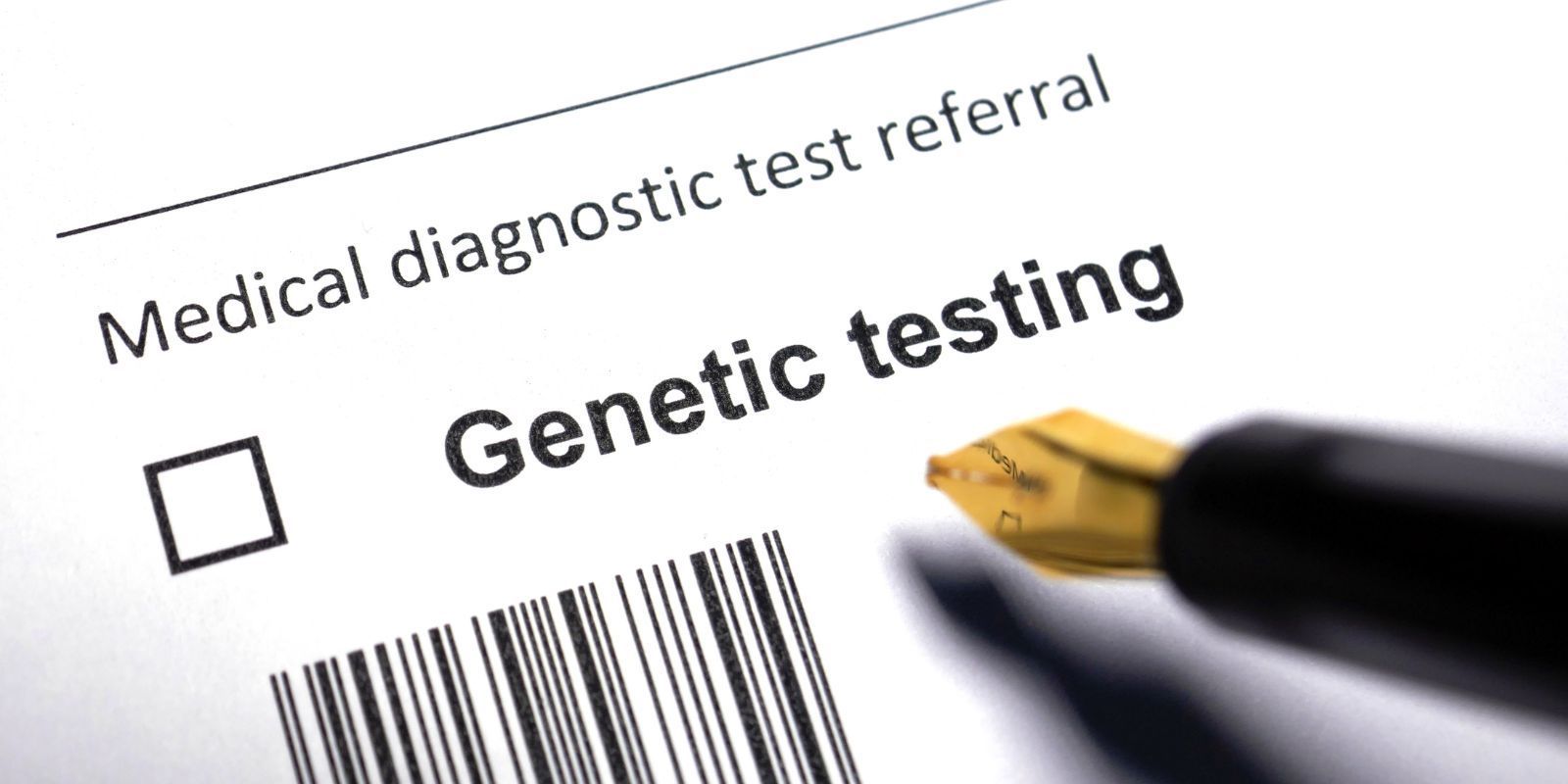 Medical diagnostic test referral form with “Genetic testing” text, checkbox, and barcode, held by a pen