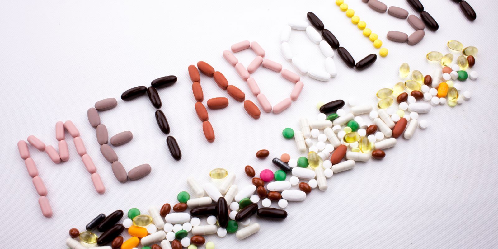 Colorful pills spelling “METABOLISM” on a white background, with scattered capsules below.