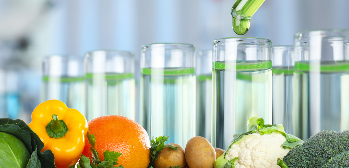 Laboratory glassware with green liquid and fresh fruits and vegetables in the foreground