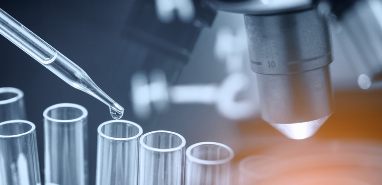 Pipette dispensing liquid into test tubes beside a microscope in a lab