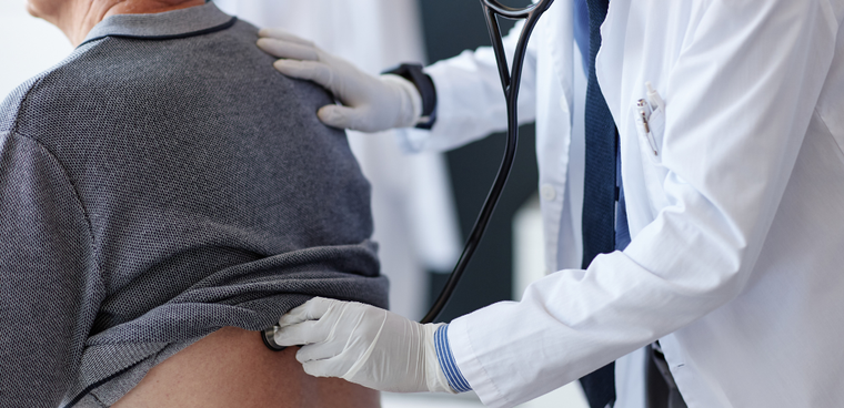 Doctor examining patient’s back with a stethoscope in a clinical setting