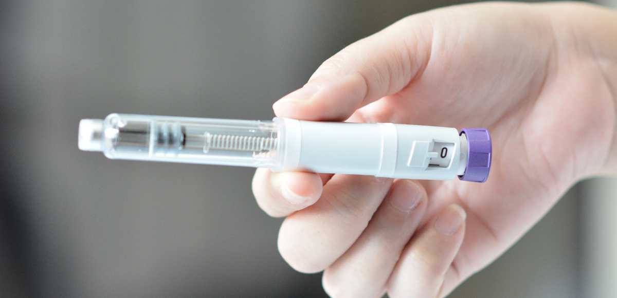 Hand holding a syringe with a purple cap against a blurred background