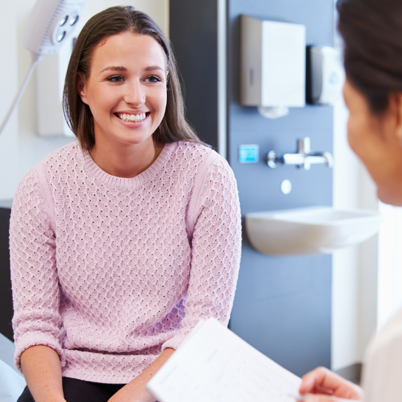 Smiling woman in a pink sweater talking with a clinician in a medical exam room