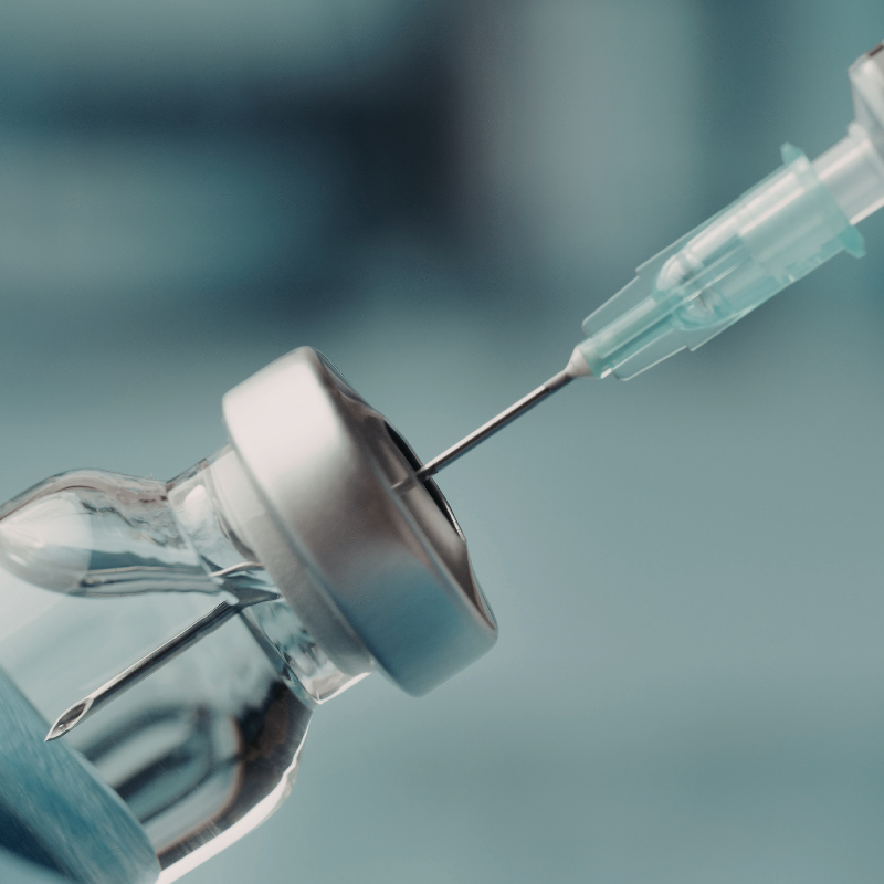 Close-up of a syringe piercing a vaccine vial stopper