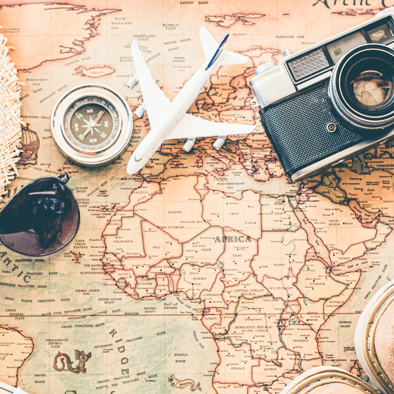 Travel gear on a world map: camera, compass, sunglasses, and toy airplane.