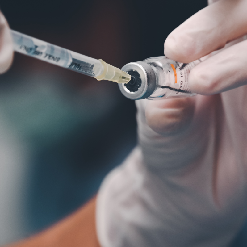 Gloved hand holding syringe and vial, drawing liquid medication into the needle