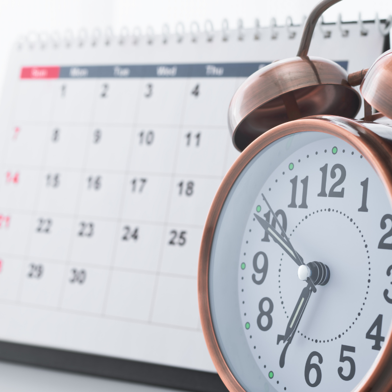 Alarm clock in front of a wall calendar, suggesting a reminder or scheduled time