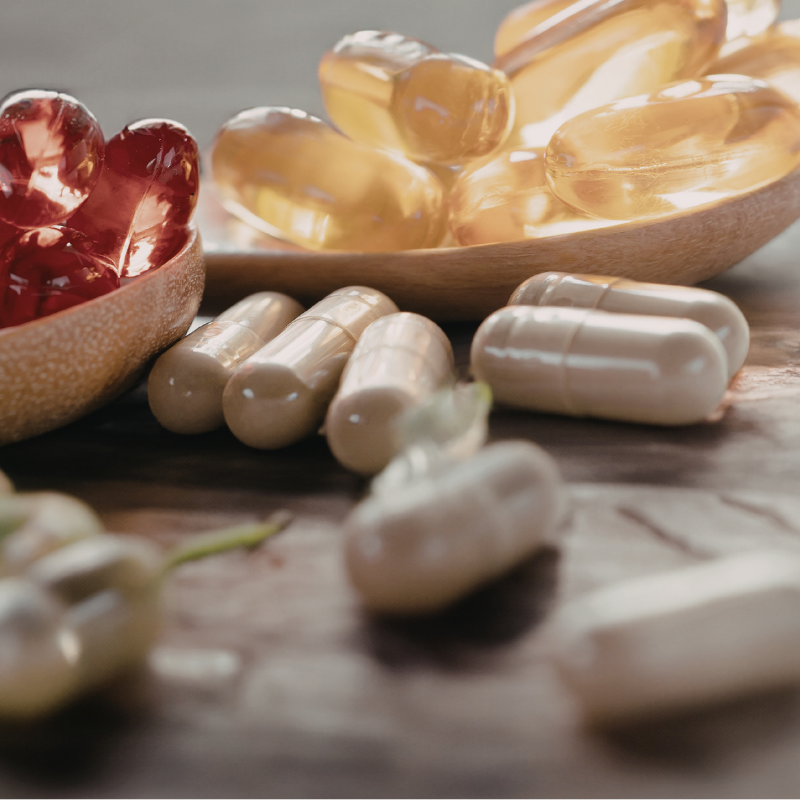 Assorted capsules and softgel pills in bowls on a wooden surface