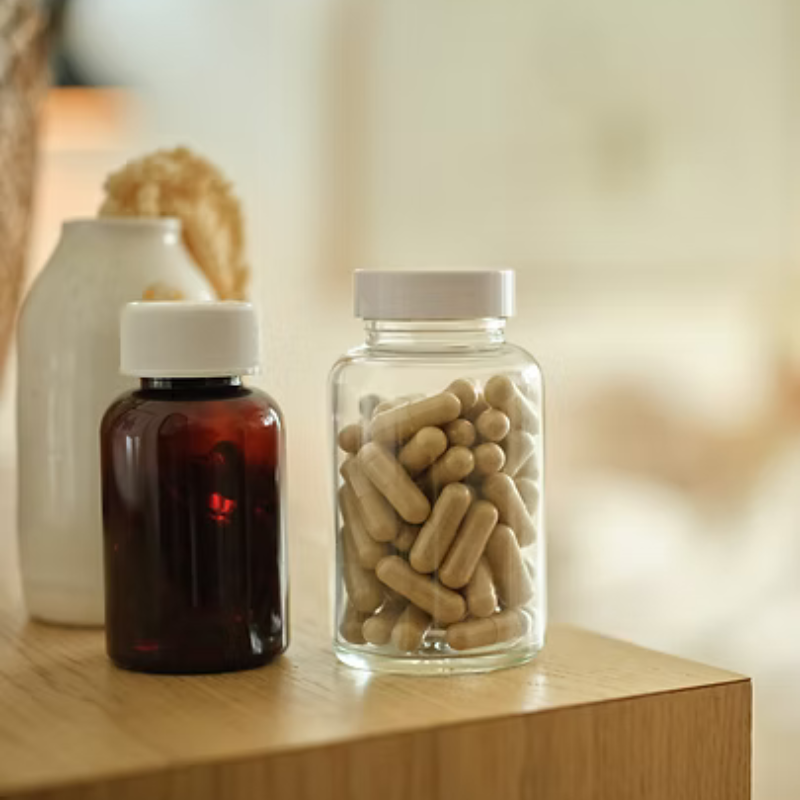 Two supplement bottles on a wooden table, one amber and one clear filled with capsules.