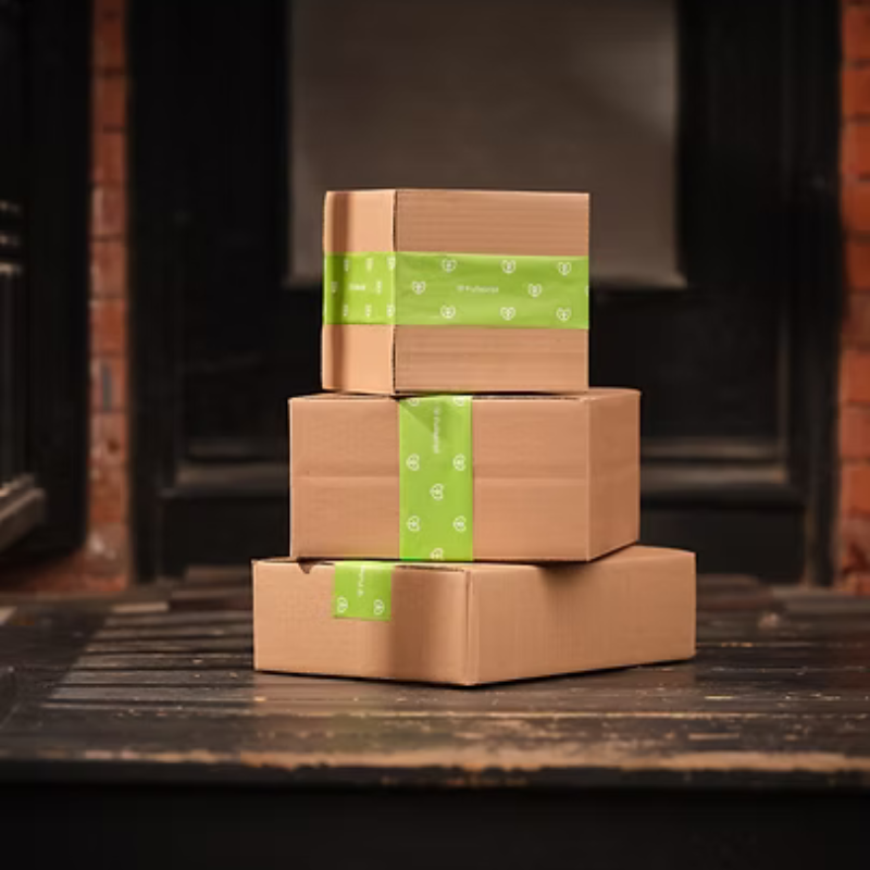 Three stacked brown gift boxes tied with green ribbon on a wooden surface