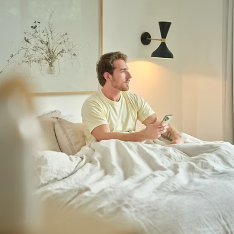 Man sitting in a bed, holding a phone in a bright, minimalist bedroom