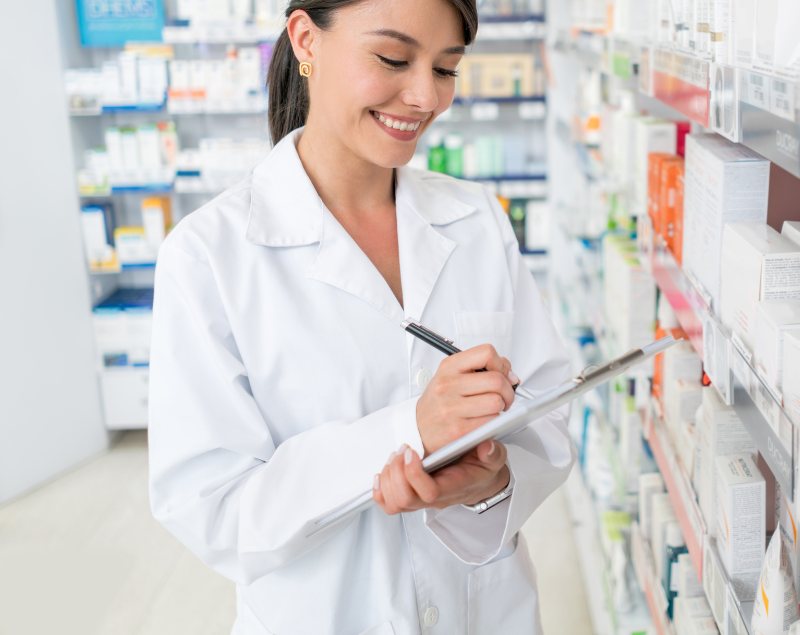 Pharmacist in white coat writing on a clipboard in a pharmacy aisle