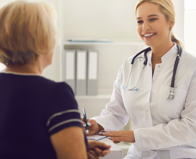 Doctor smiling while checking a patient's blood pressure in a bright clinic room