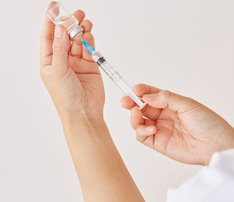 Hands drawing liquid from a vial into a syringe on a white background