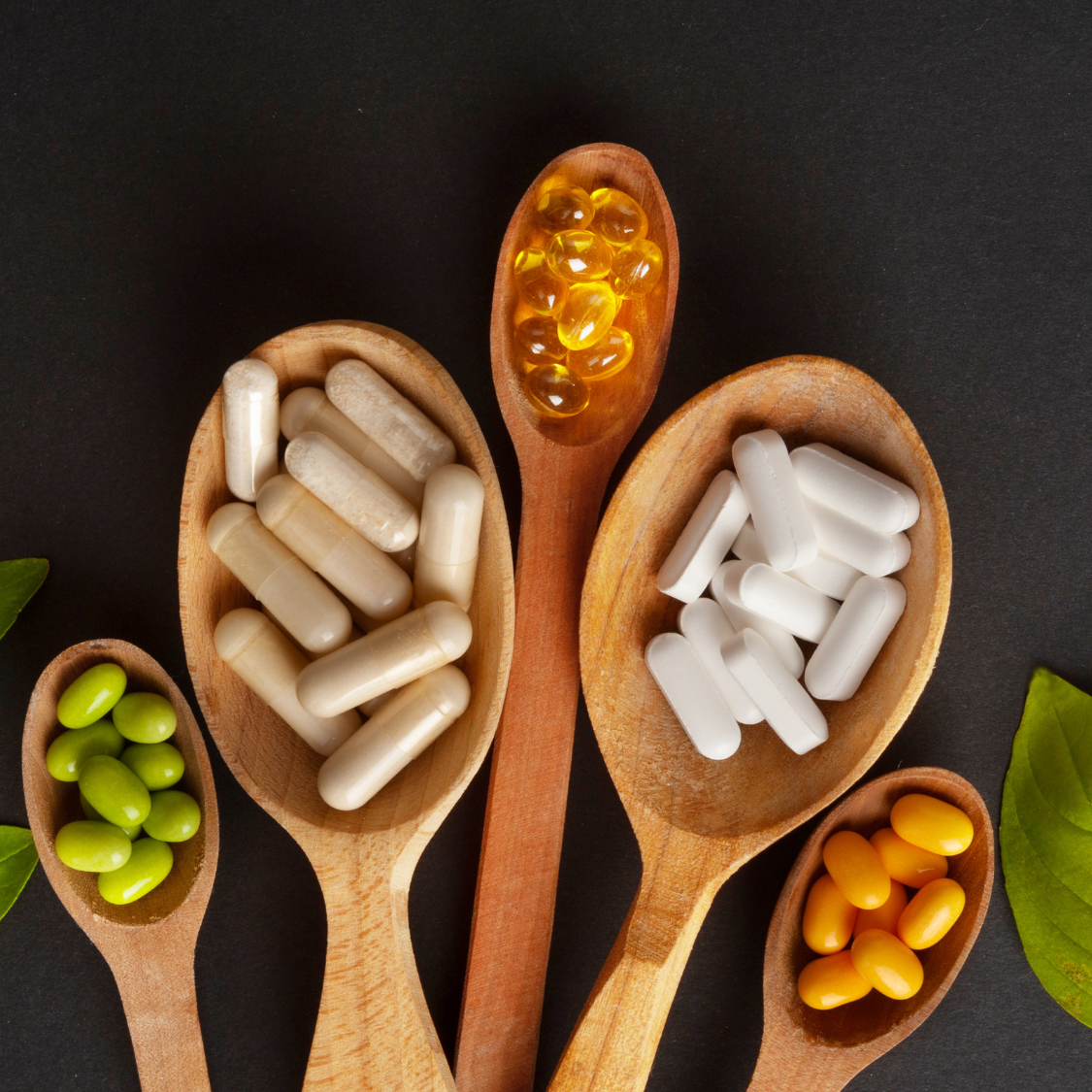 Wooden spoons holding assorted colorful pills and capsules on a dark background