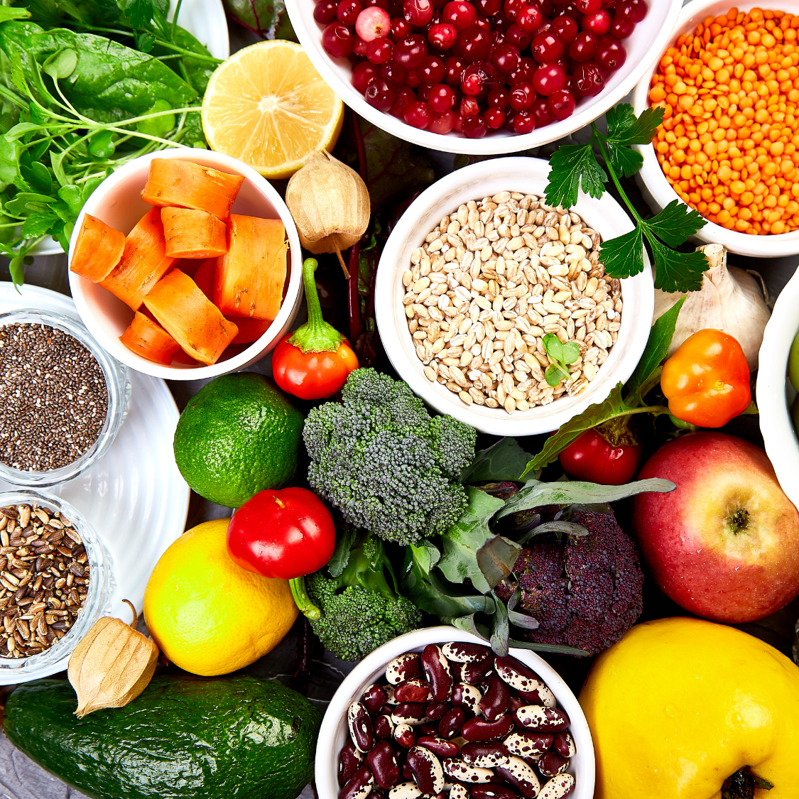 Assorted fresh fruits and vegetables, including citrus, berries, pumpkins, broccoli, and beans, arranged on a white table.