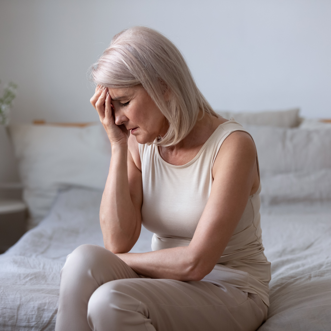Woman sitting on a bed with head in hand, looking distressed in a softly lit bedroom