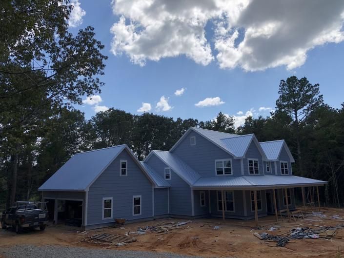 New gray house under construction with front porch, surrounded by trees under a blue sky