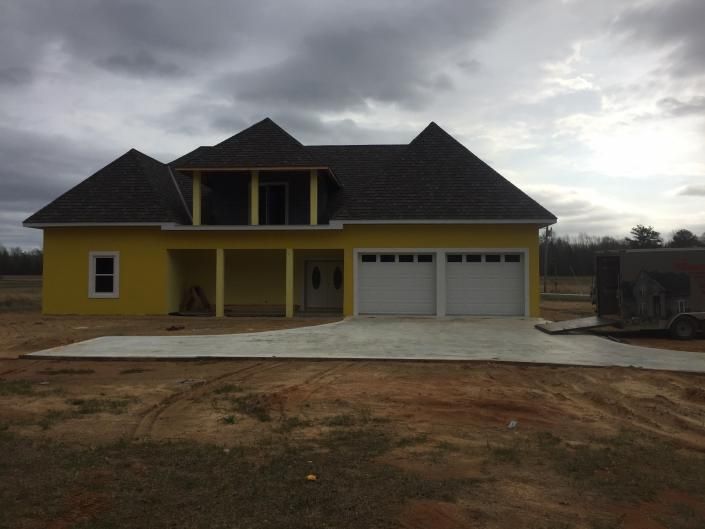 Yellow two-story house with dark roof and double garage under cloudy sky