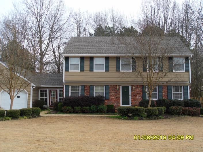 Two-story beige house with blue shutters, red door, and a detached garage in a suburban yard