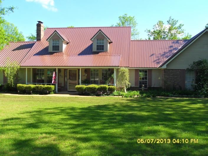Red house with a red metal roof, dormer windows, and a large green lawn on a sunny day