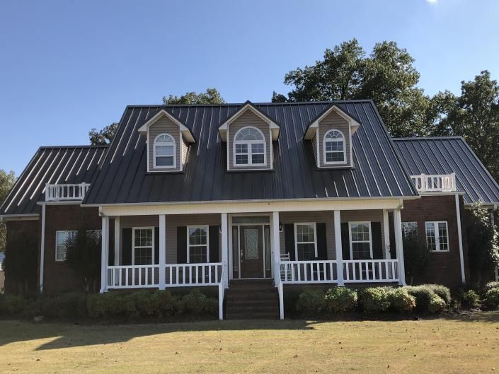 White two-story house with dark roof, dormer windows, and a front porch on a grassy lawn