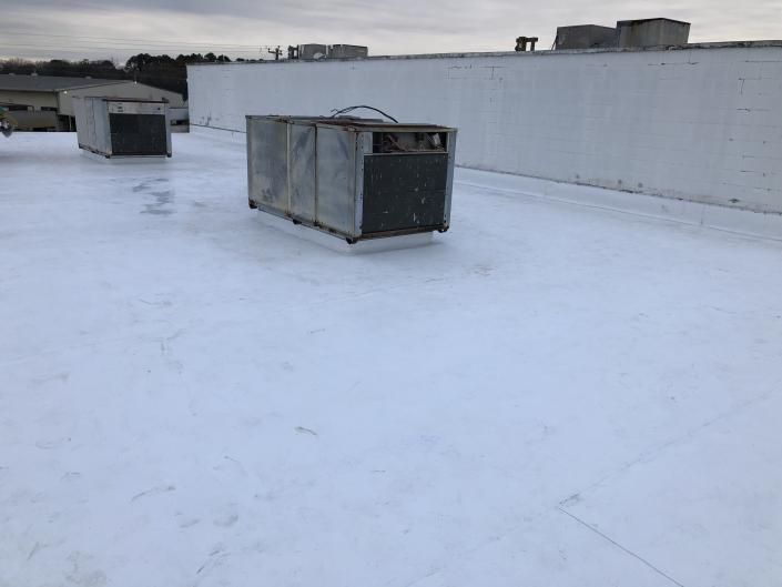 Flat white rooftop with HVAC units and a low parapet wall under an overcast sky