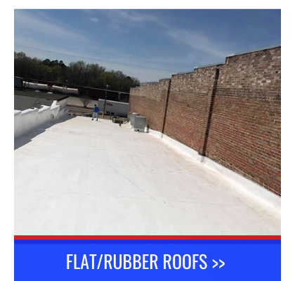 Flat white rubber rooftop with brick wall and worker in the distance under blue sky