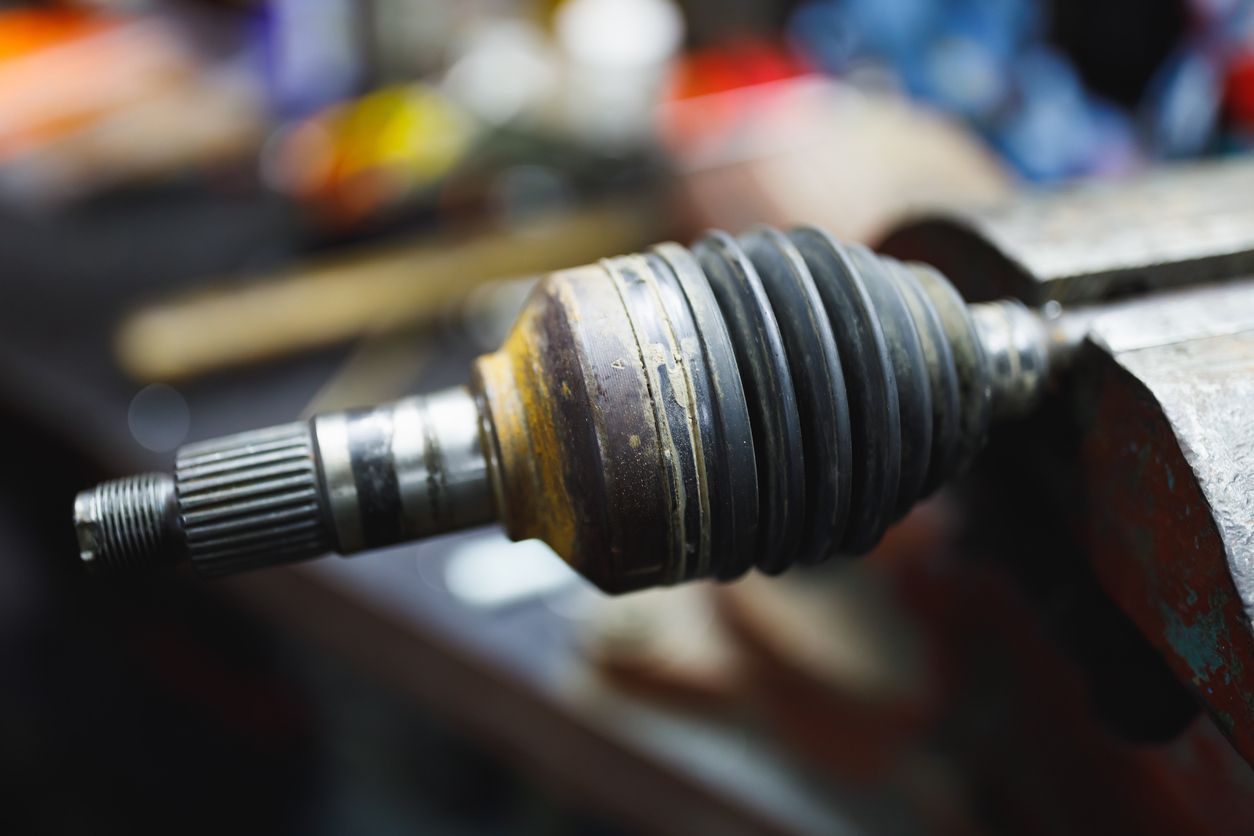 Close-up of a dirty metal car axle joint on a workbench, with blurred tools in the background