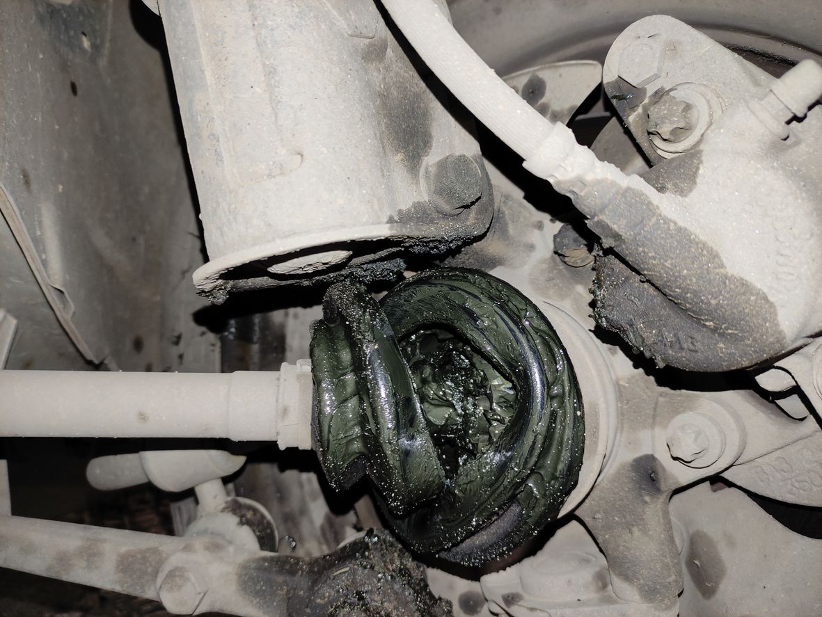 Grease-covered suspension joint on a vehicle underside, with dark green lubricant and white dusty components.