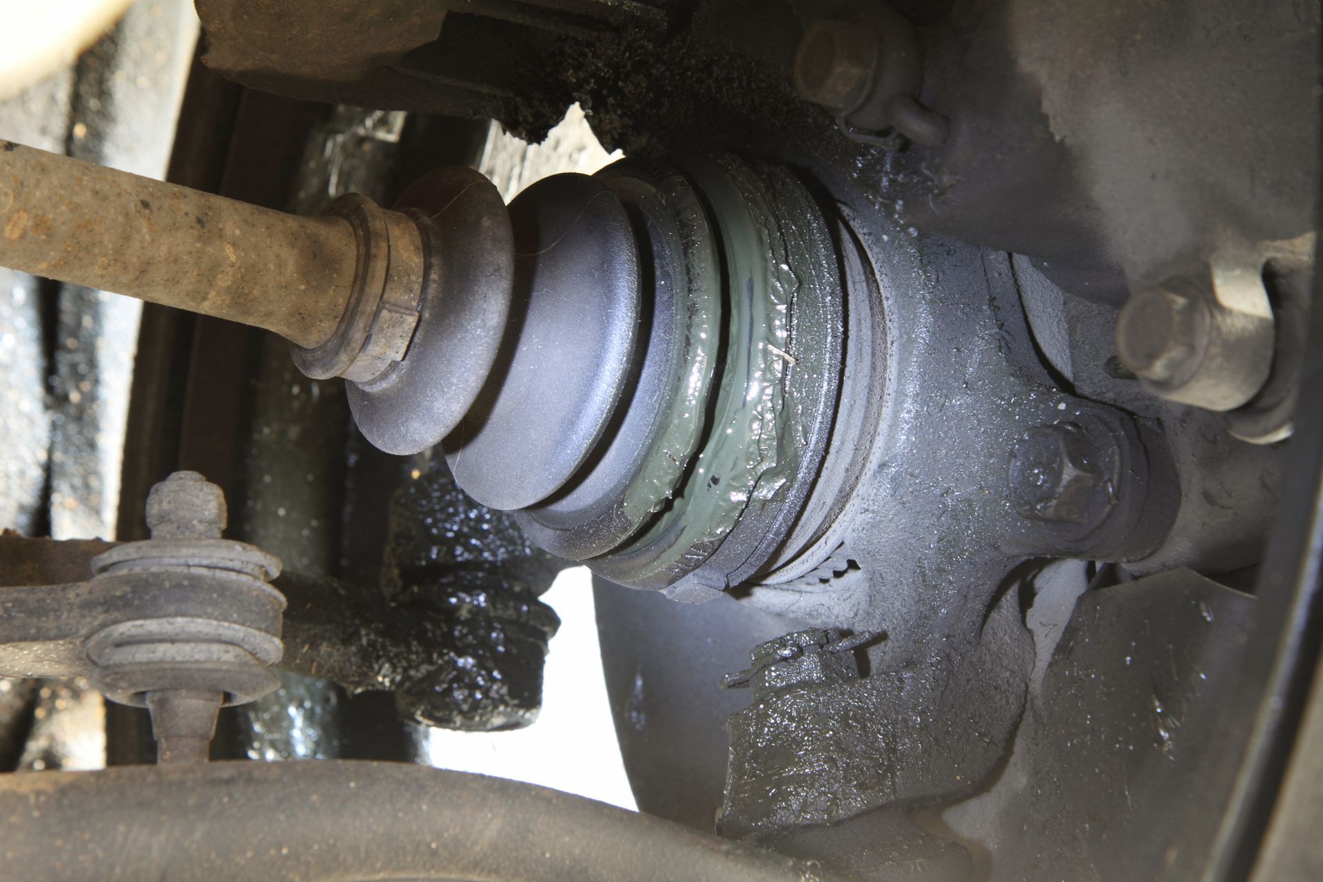 Close-up of a car CV axle and wheel hub with grease leaking around the joint