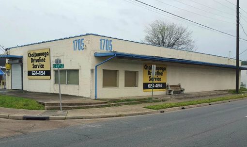 Corner storefront with tan walls and blue trim, featuring yellow signs on a street corner.