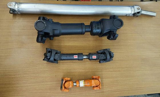 Four metal drive shafts of varying sizes laid horizontally on a wooden surface.