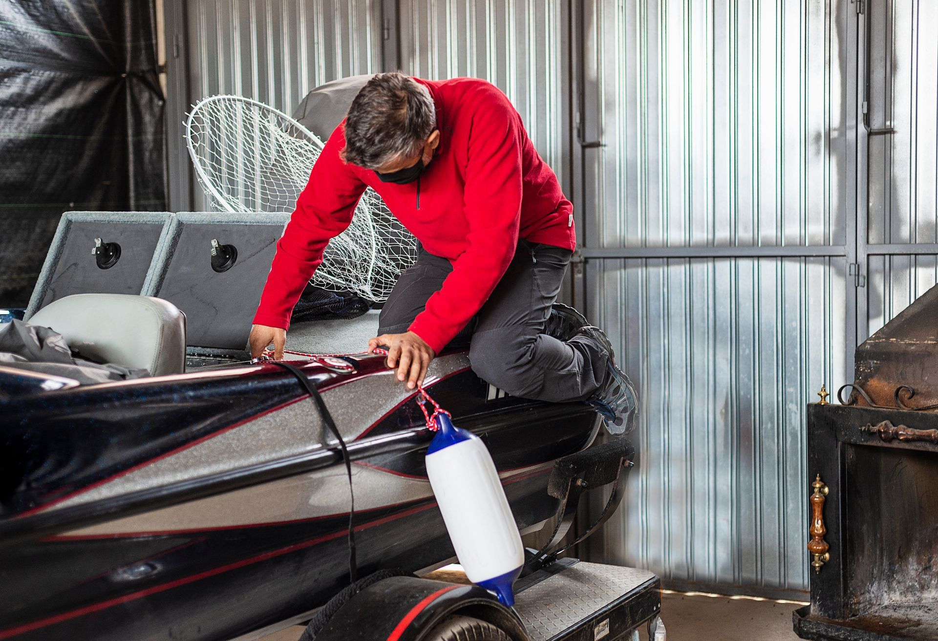 Person in red top cleaning a black boat with a spray bottle in a workshop
