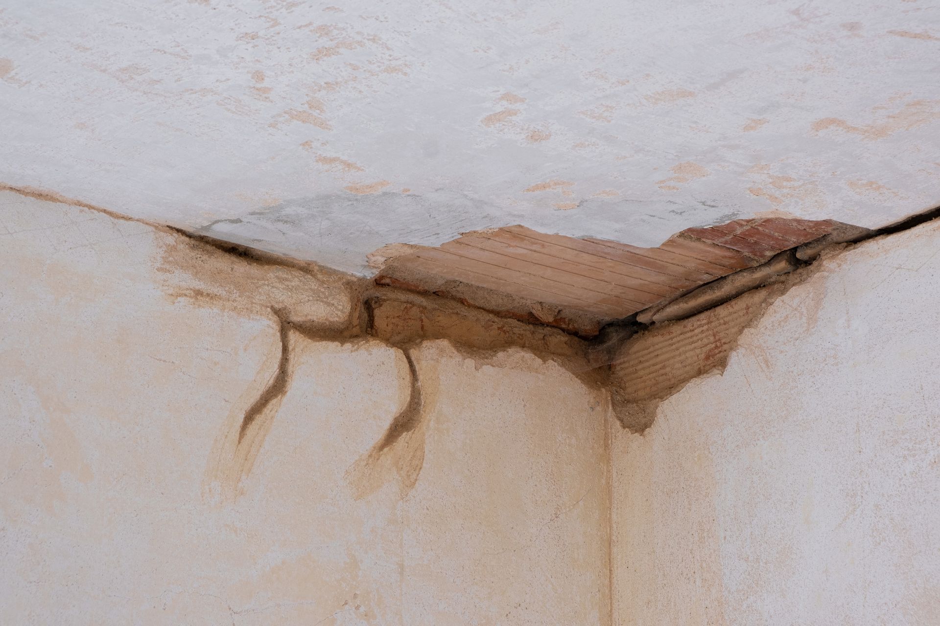 Water-damaged ceiling corner with exposed wood lath and dark stains.
