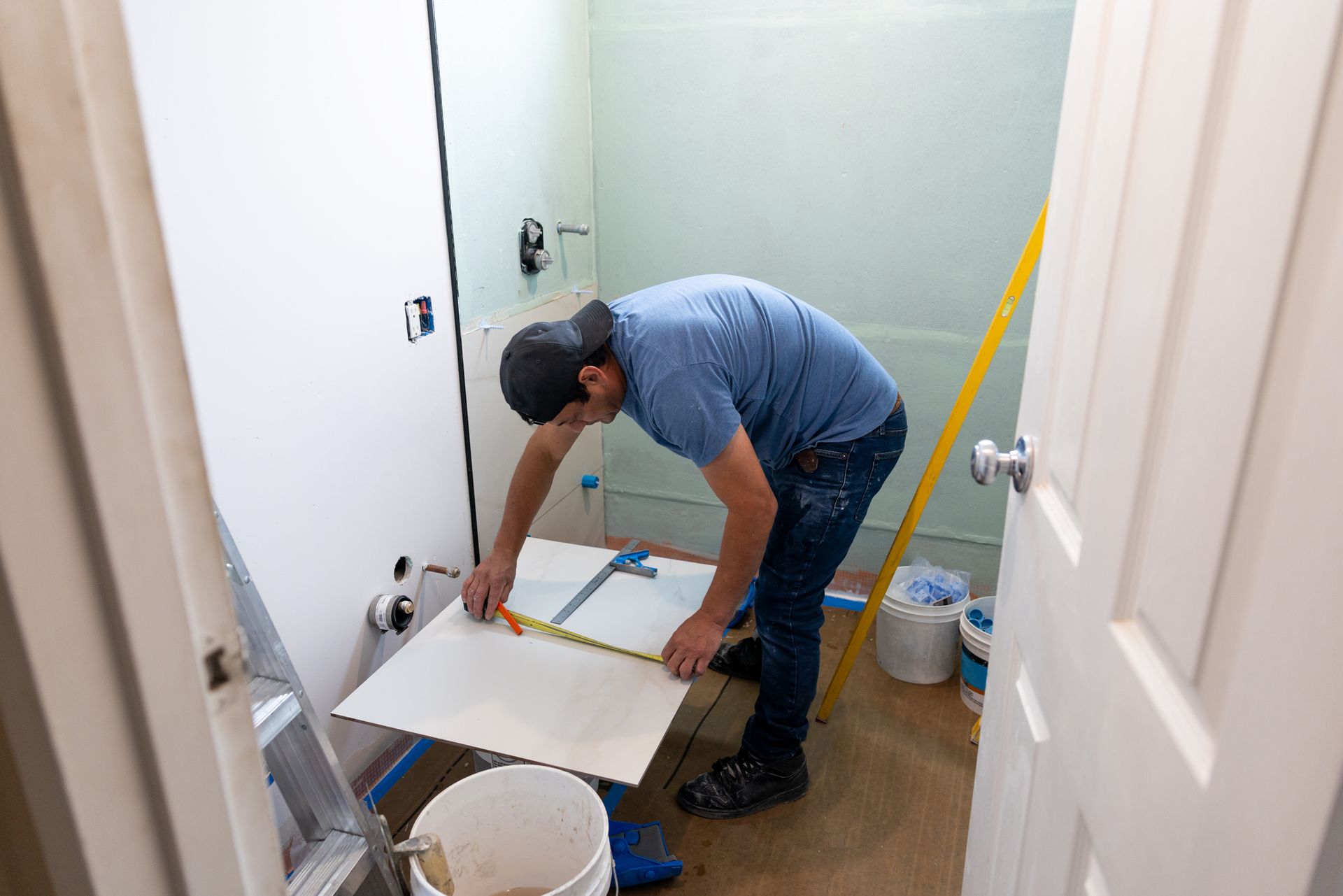 A worker measuring a tile with a tape measure during bathroom renovation
