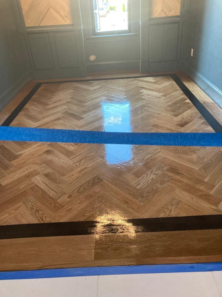 A wooden floor with a herringbone pattern and a blue tape.
