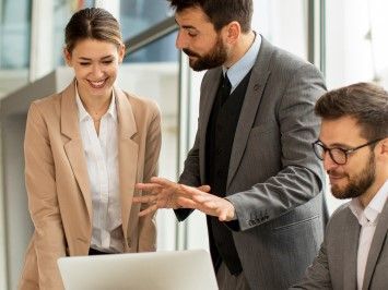 a group of business people are standing around a laptop computer .