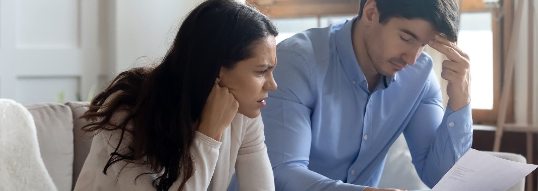 a man and a woman are sitting on a couch looking at a piece of paper .