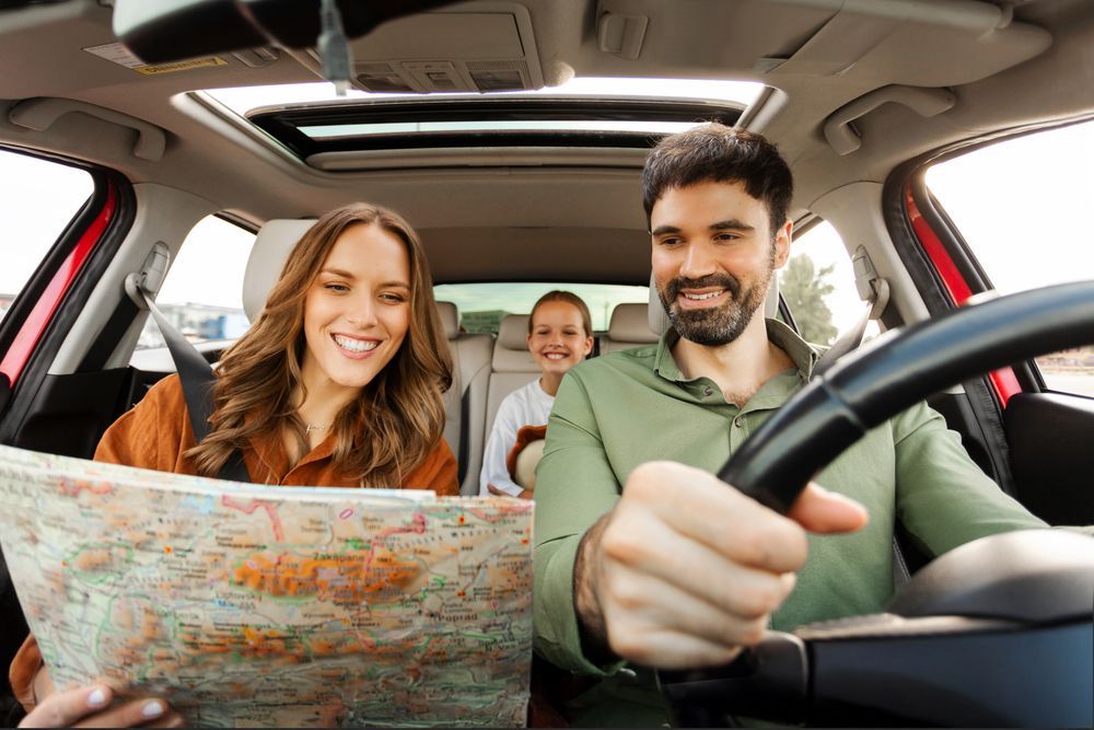 Tres personas sonriendo en un coche, leyendo un mapa durante un viaje por carretera.