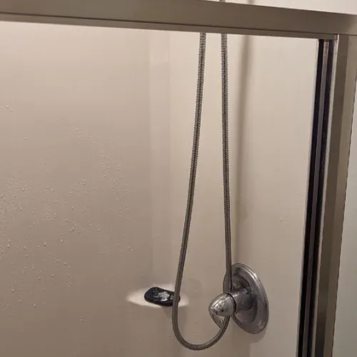 A shower head is hanging from a shower door in a bathroom | The Duke Of Plumbing