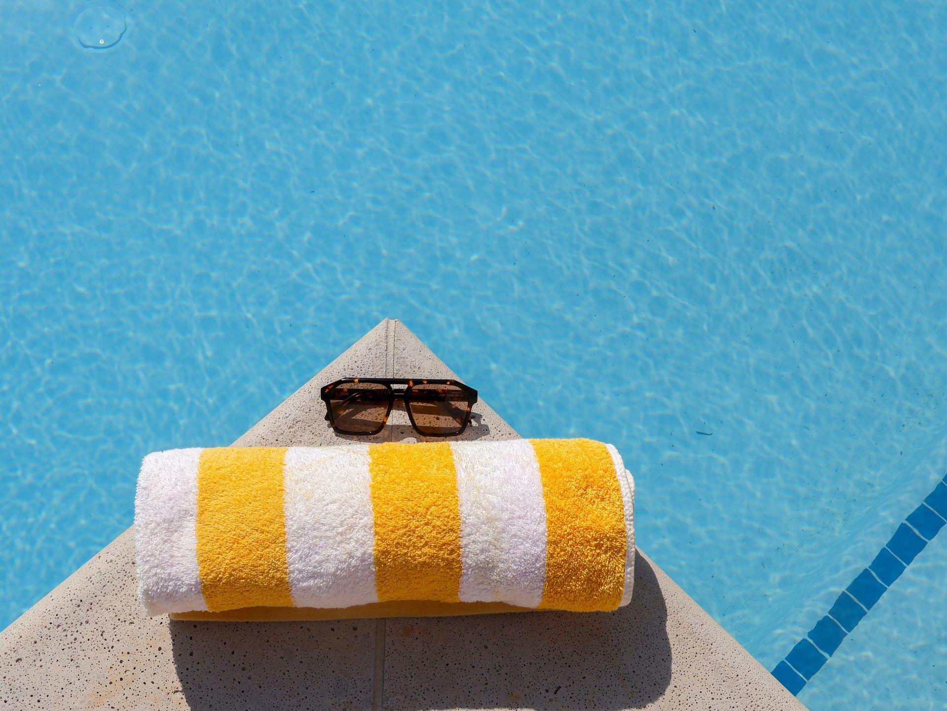 Towel and sunglasses on a sun lounger by a blue swimming pool