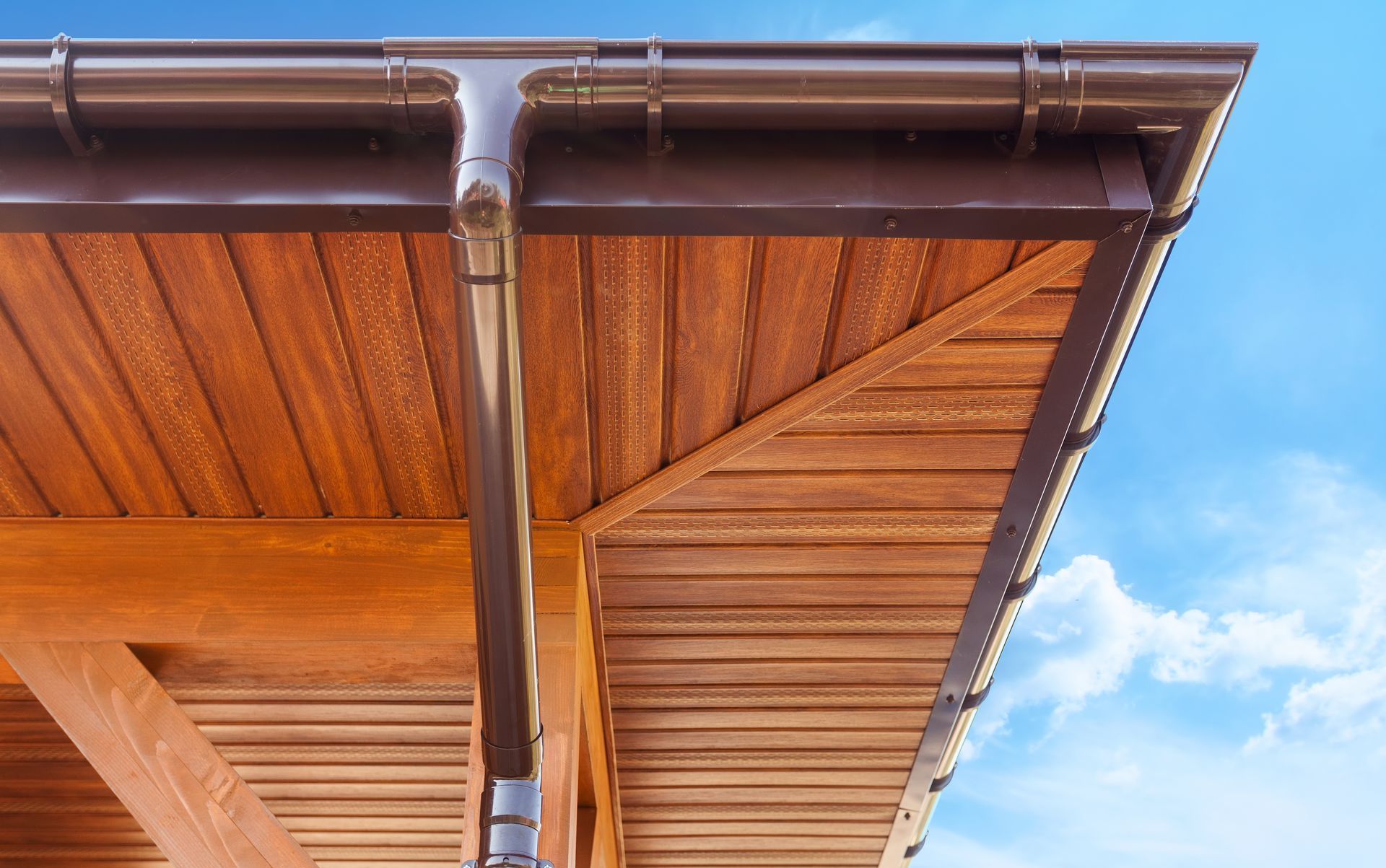 a wooden roof with a brown gutter and a blue sky in the background .