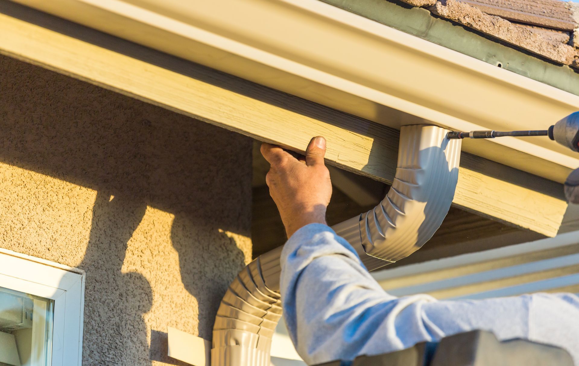a man is fixing a gutter on a house with a drill .