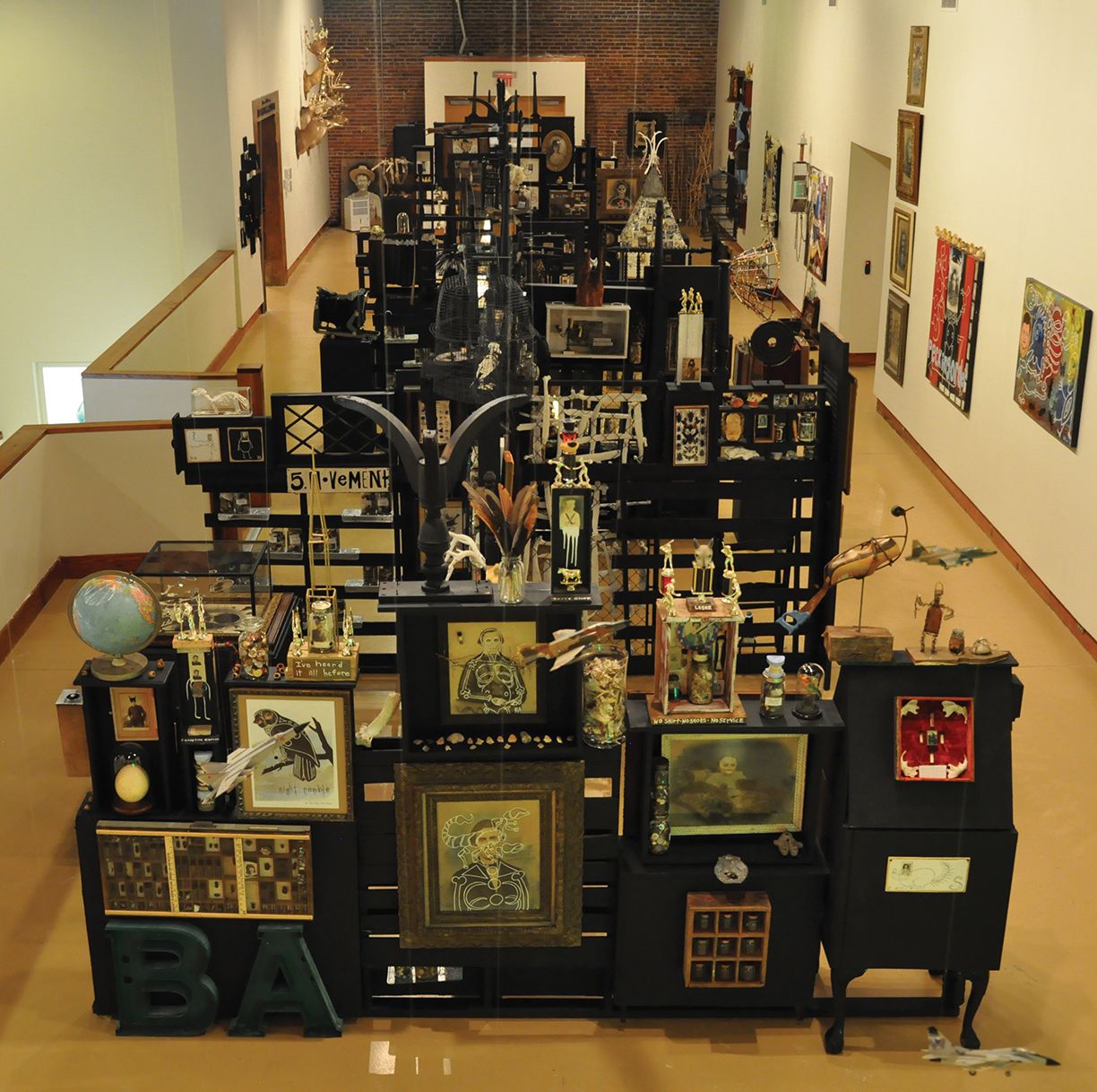 Gallery room filled with dense rows of framed artworks and display cases along a long aisle