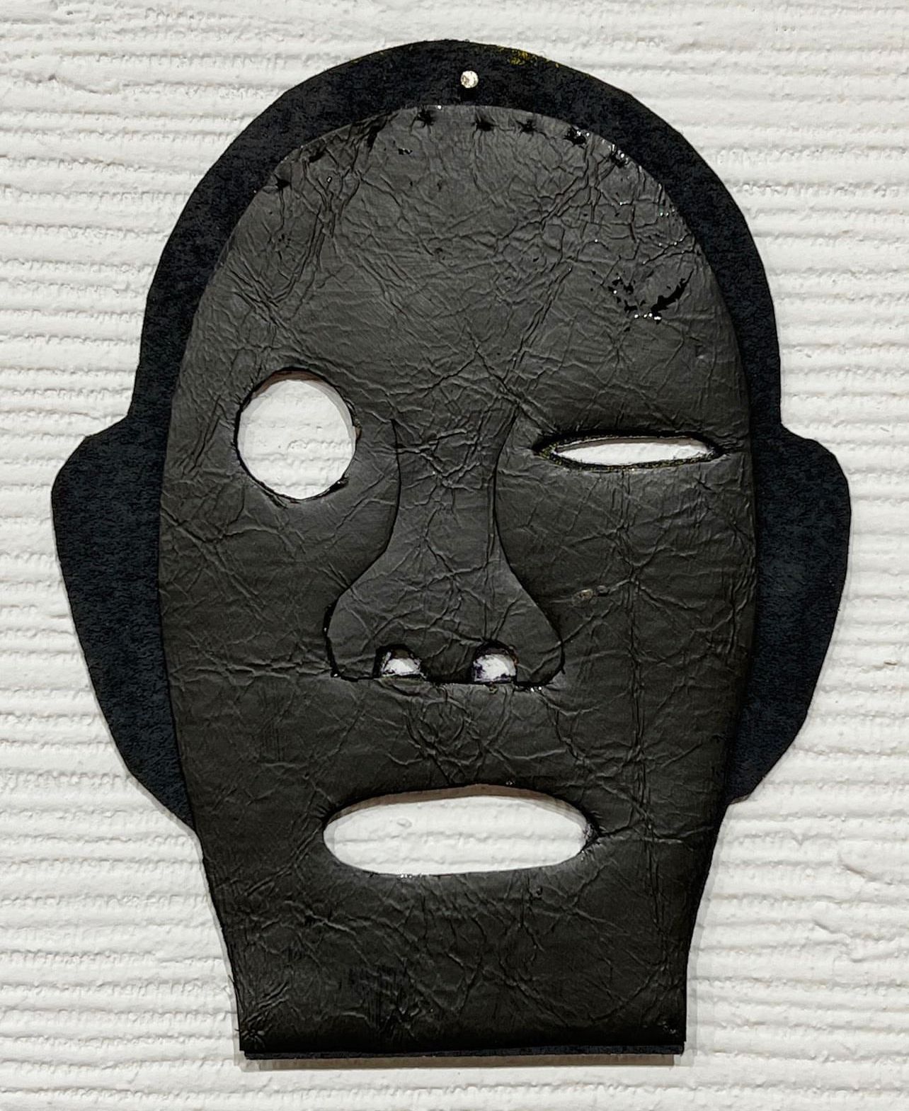 Black face mask with cutout eyes and mouth on a light textured background