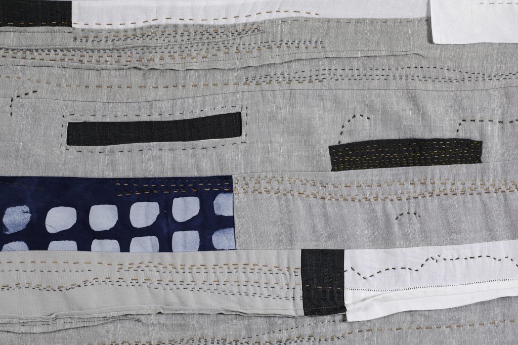 Close-up of a gray fabric with black rectangular patches and blue patterned trim around handwritten markings